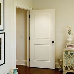 there is a white door in the hallway with pictures on the wall and vases next to it