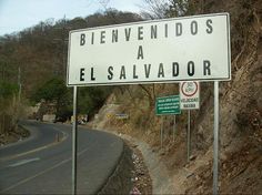 a street sign on the side of a road near a hill with trees in the background