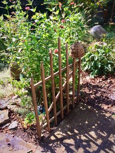 a wooden fence made out of sticks and some plants in the back yard with flowers growing behind it