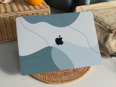 an apple laptop sitting on top of a table next to some oranges and a wicker basket