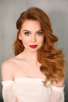 a woman with long red hair and blue eyes wearing a white off the shoulder dress