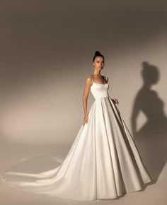 a woman in a white wedding dress posing for the camera with her shadow behind her