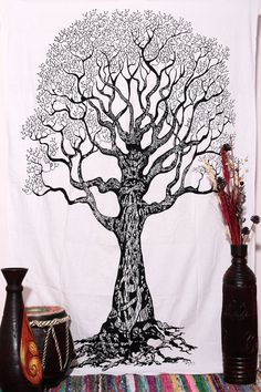 a white wall hanging with a black tree on it and vases next to it