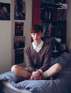 a young man sitting on top of a bed next to a book shelf filled with books