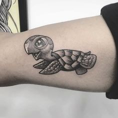 a small turtle tattoo on the left forearm and arm, with an eyeball in it's mouth