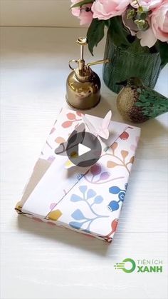 an open book sitting on top of a table next to pink flowers and a vase