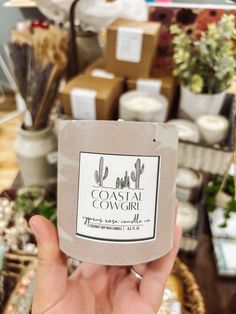 a hand holding up a jar of clay that says coastal cowgirl in front of some plants