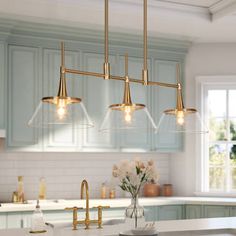 a kitchen with blue cabinets and white countertops, gold fixtures and pendant lights hanging from the ceiling