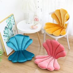 three different color shell shaped cushions sitting on the floor next to a white table and chair