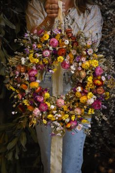 A woman holding a colourful wreath made with native daisies and wildflowers Flowers Australia, Circle Wreath, Wild Grasses, Wildflower Wreath, Newcastle Nsw, Seed Heads, Dried Flower Wreaths, Sustainable Decor