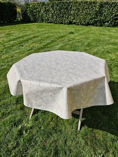 a white table cloth sitting on top of a lush green grass covered field next to a hedge