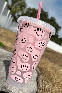 a pink cup with smiley faces on it and a straw sticking out of the lid