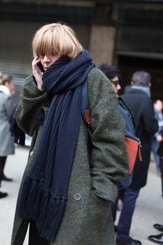 a woman is talking on her cell phone while wearing a scarf and coat with pockets