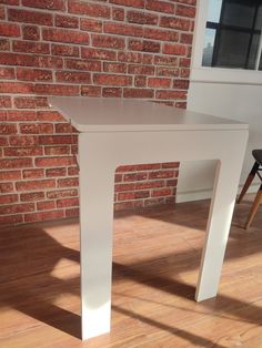 a white table sitting on top of a hard wood floor next to a brick wall