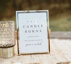 a close up of a sign on a table near a cup and vase with a candle