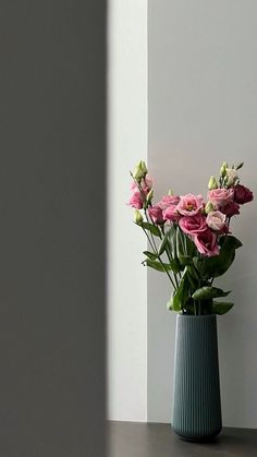 a vase with pink flowers sitting on a table in front of a white wall and window