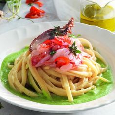 a white plate topped with pasta and vegetables on top of green sauce next to olive oil