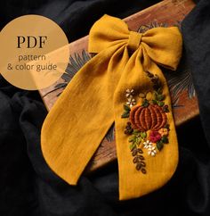 a yellow bow tie sitting on top of a wooden board with flowers and leaves embroidered on it