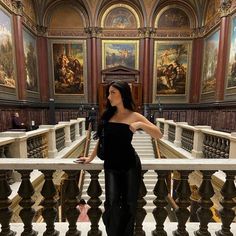 a woman standing on top of a stair case in a building with paintings on the walls