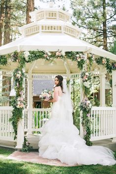 a bride standing in front of a gazebo with flowers and greenery on it