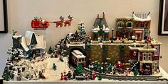 a lego christmas village is shown in front of a white wall and framed pictures on the wall