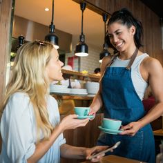 two women in aprons are talking to each other while holding cups and spoons