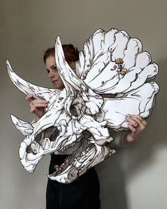 a woman is holding up a paper cutout of a skull with large, white flowers on it