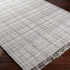 a white rug with fringes on top of a wooden floor in an empty room