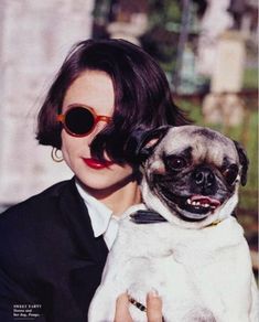 a woman holding a pug in her arms and wearing sunglasses on top of her head