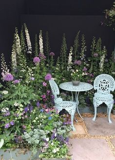 two chairs and table sitting in front of some flowers