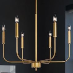 a gold chandelier with six candles hanging from the ceiling in front of a black wall