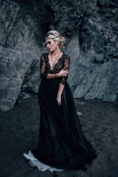 a woman in a black dress is standing by some rocks