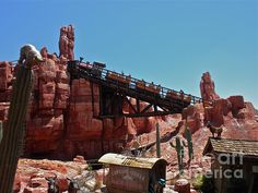 a train going over a bridge in the middle of a rocky area with cacti