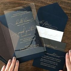 two hands are holding an open book on top of a table with wedding stationery