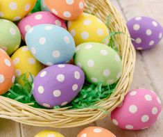 painted easter eggs in a basket on a wooden table next to green grass and white polka dots