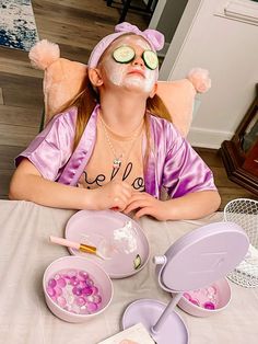 a woman with cucumbers on her face sitting at a table in front of bowls