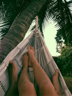 two people laying in a hammock under a palm tree with their feet propped up