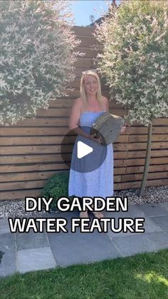 a woman standing in front of a wooden fence holding a piece of paper with the words diy garden water feature