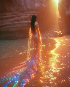 a woman is standing in the water wearing a long dress with colorful lights on it