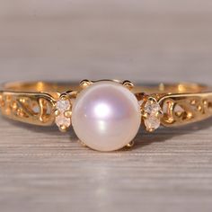 a close up of a ring with a pearl and diamonds on the front, sitting on a wooden surface