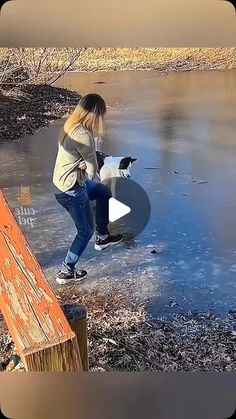 a woman is playing with her dog on the ice covered ground near a body of water