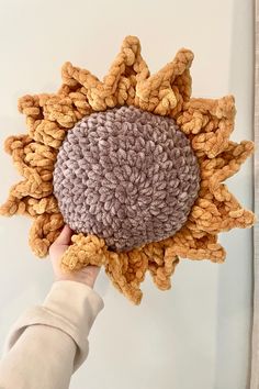 a hand holding a crocheted sunflower in front of a white wall