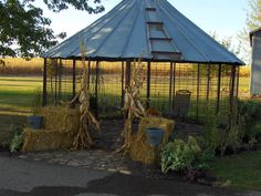 two scarecrows sitting on hay in front of a gazebo with corn stalks growing out of it