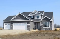 a large house with two garages and three windows on the front of it, surrounded by dirt