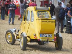 a small yellow car parked in the middle of a field with people standing around it