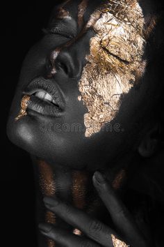 a woman with black and gold face paint on her face, holding her hand to her cheek