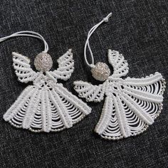 two white angel ornaments are hanging from strings on a black cloth surface, one is decorated with beads and the other has beading