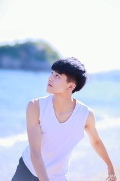 a young man standing on top of a beach next to the ocean wearing a white shirt