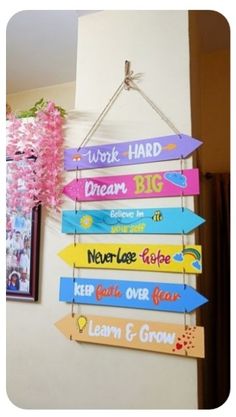 a wooden sign hanging from the side of a wall next to a pink flower and framed photo