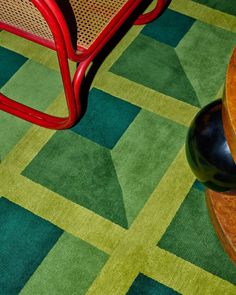 a red chair sitting on top of a green rug next to a wooden table with a black ball